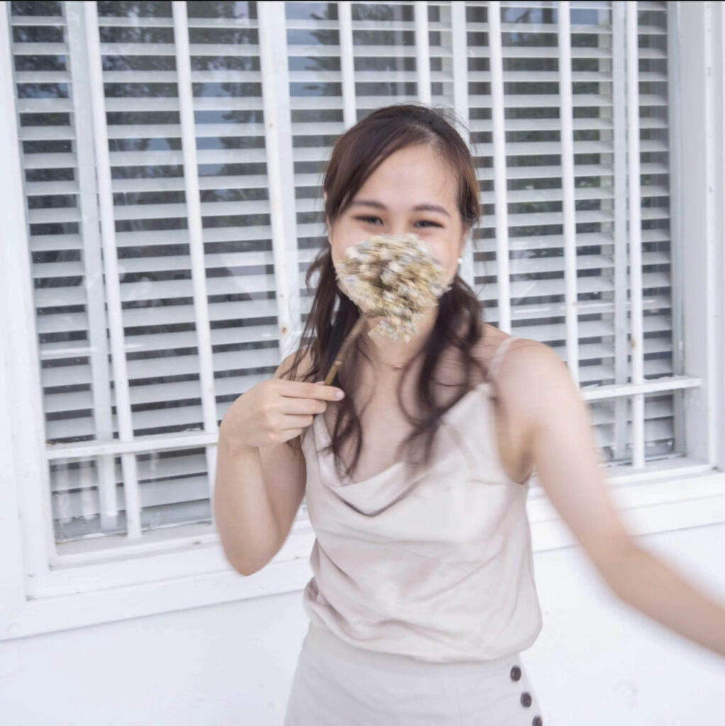 Jasmine wearing all cream and golden , with a dried flower over her nose.