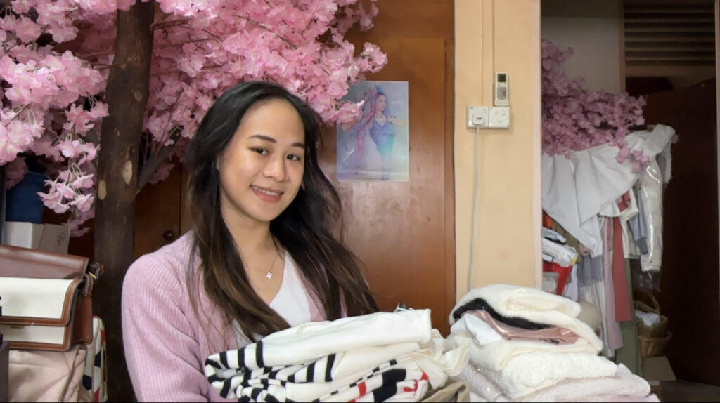 Founder of Jassydarling blog, Jasmine is smiling, holding a pile of clothes of fashion items in her hand, pink flowers in the background.